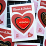 A close-up of several enamel heart-shaped pins mounted on branded display cards. The central pin is bright red with a black outline and the word 'NEGRONI' in white.
